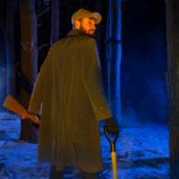 Shotgun and shovel wielding man alone in misty dark forest at night